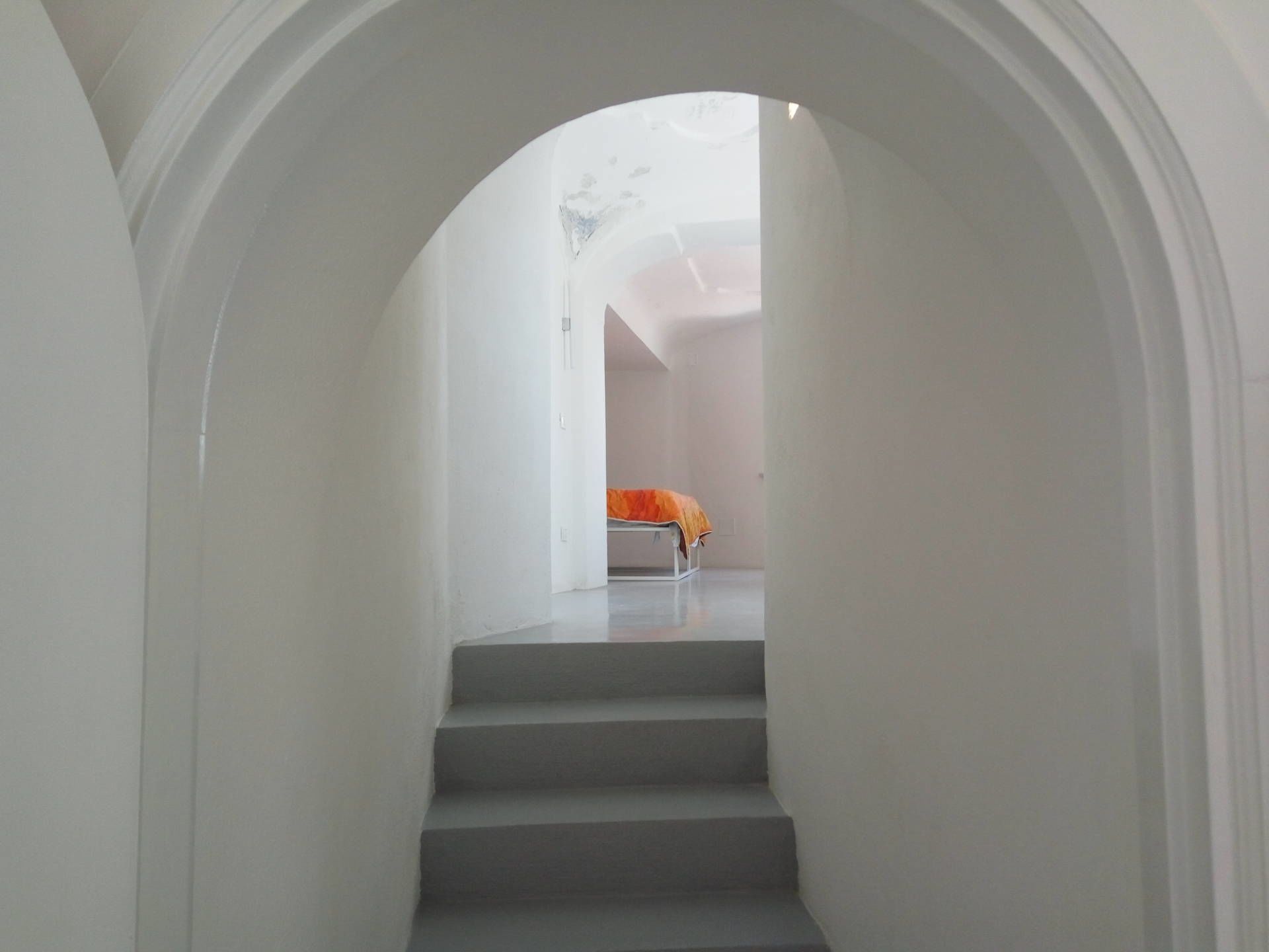 A narrow, white-walled hallway with a staircase leading to a room.