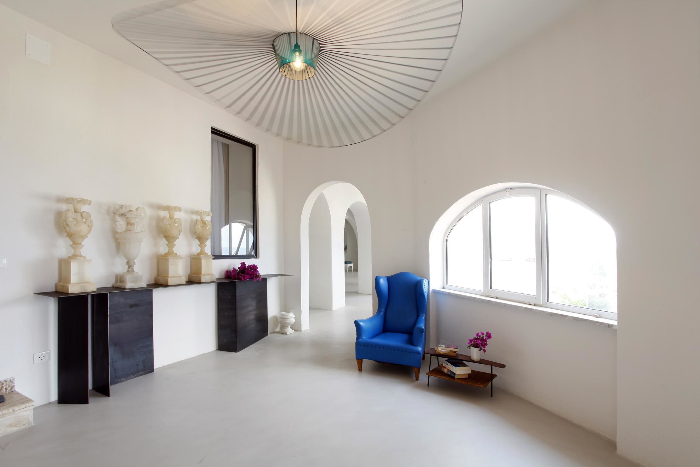 Une pièce spacieuse avec une grande fenêtre, un fauteuil bleu et un ventilateur de plafond.