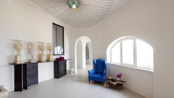 Une pièce spacieuse avec une grande fenêtre, un fauteuil bleu et un ventilateur de plafond.