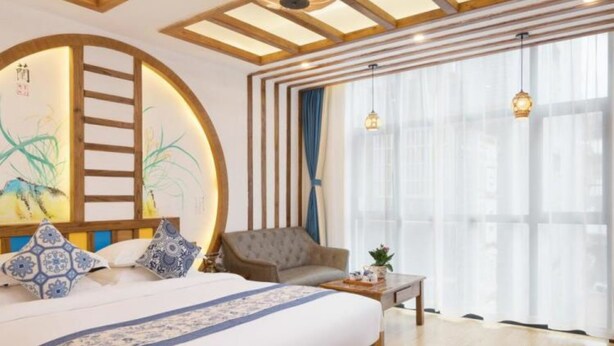 A spacious bedroom with a large bed, a wooden ceiling, and a view of the city through large windows. - Floral Hotel Zhangjiajie Mengqi Meiju (Zhangjiajie)