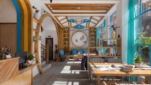 A spacious hotel lobby with wooden beams, a reception desk, comfortable seating areas, and a large window offering a view of the outdoors. - Floral Hotel Zhangjiajie Mengqi Meiju (Zhangjiajie)