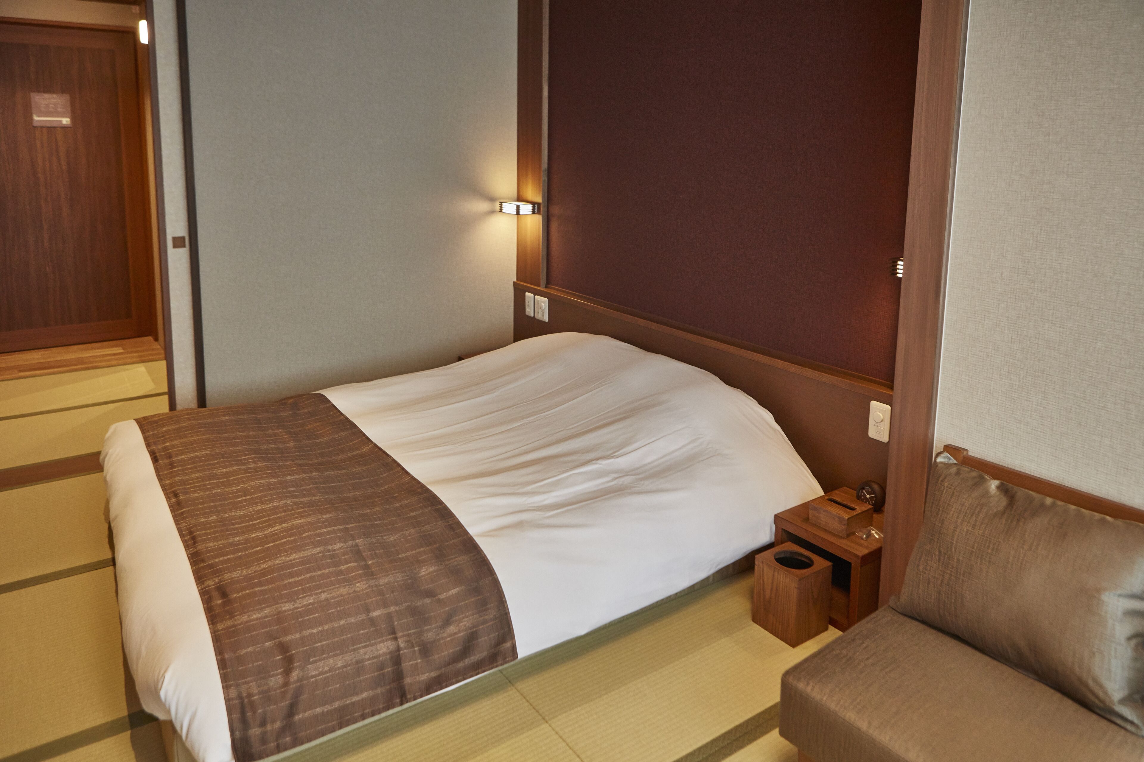 Una habitación de hotel con una cama, una mesita de noche, una pequeña mesa de madera y un sofá.