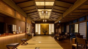Un interior tradicional japonés con suelo de tatami, mobiliario de madera y una zona de recepción con mostrador y asientos.