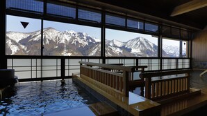 Un onsen japonés tradicional con bancos de madera y vistas a montañas nevadas a través de amplios ventanales.