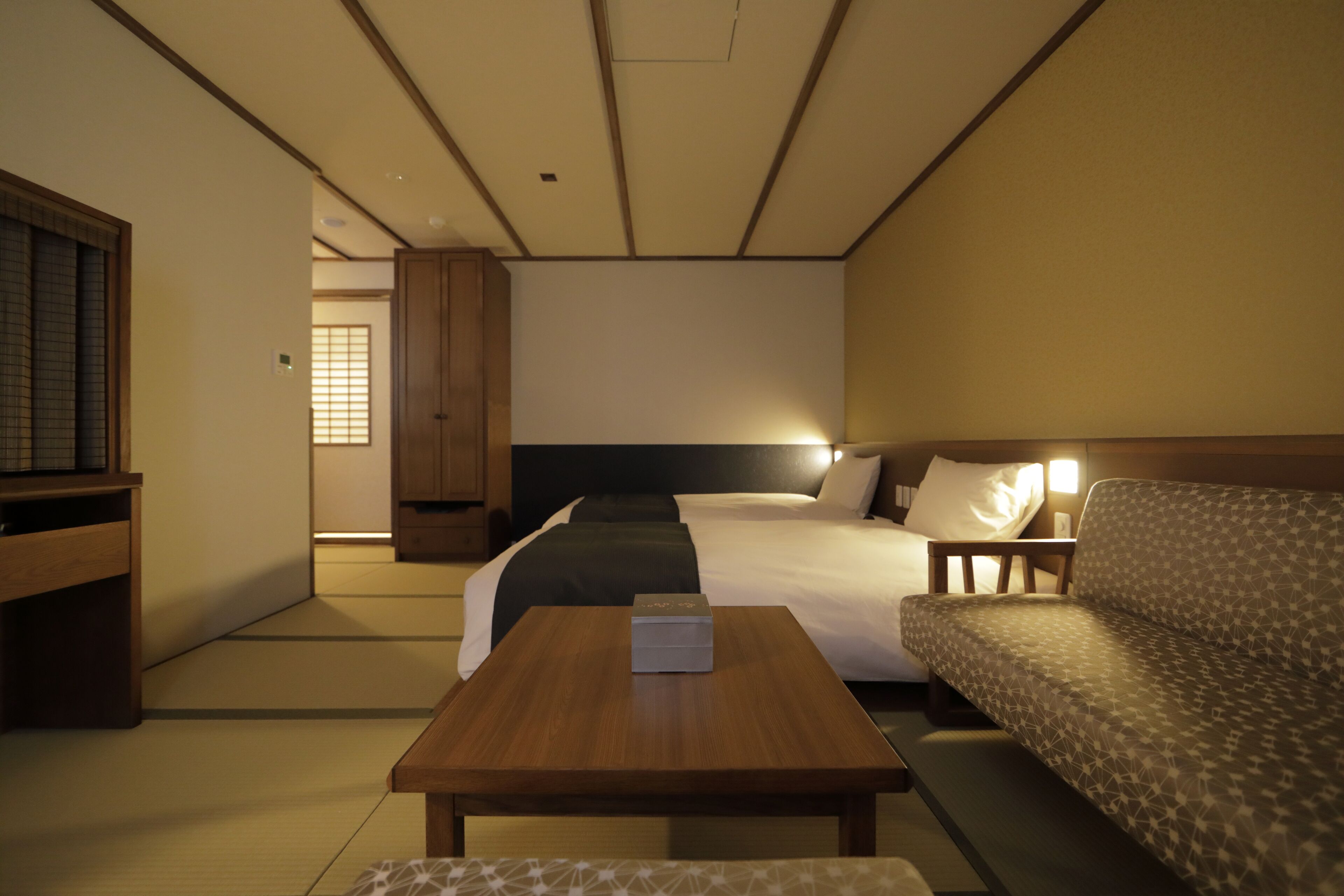 A hotel room with a bed, a sofa, a wooden table, and a TV.