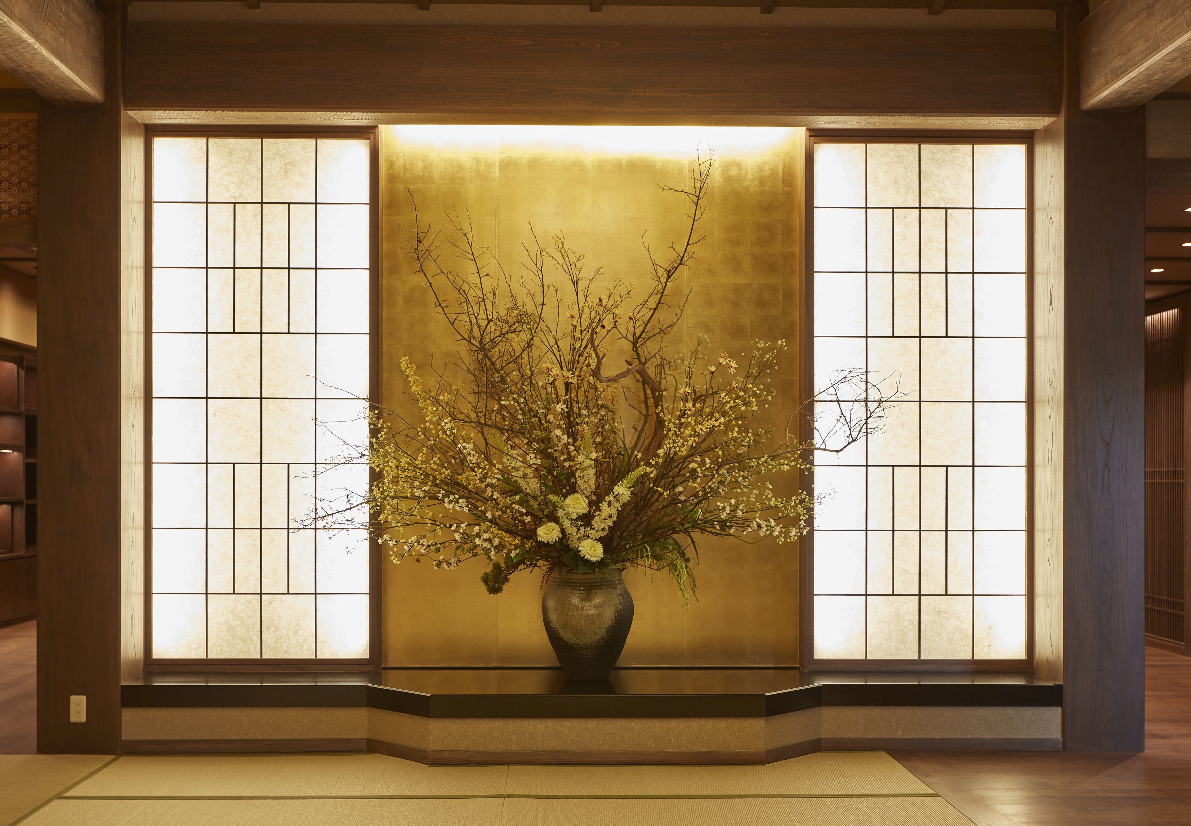 Een traditioneel Japans interieur met een tatami vloer, een houten receptiebalie en een grote bloevas.