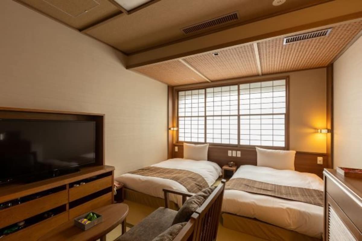 Habitación de hotel con dos camas, televisión, aparador de madera y ventana con vistas.