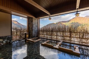 A serene indoor hot spring area with stone flooring, wooden benches, and a view of autumnal mountains through a wooden lattice. - Yukemurinoyado Yukinohana (Yuzawa)