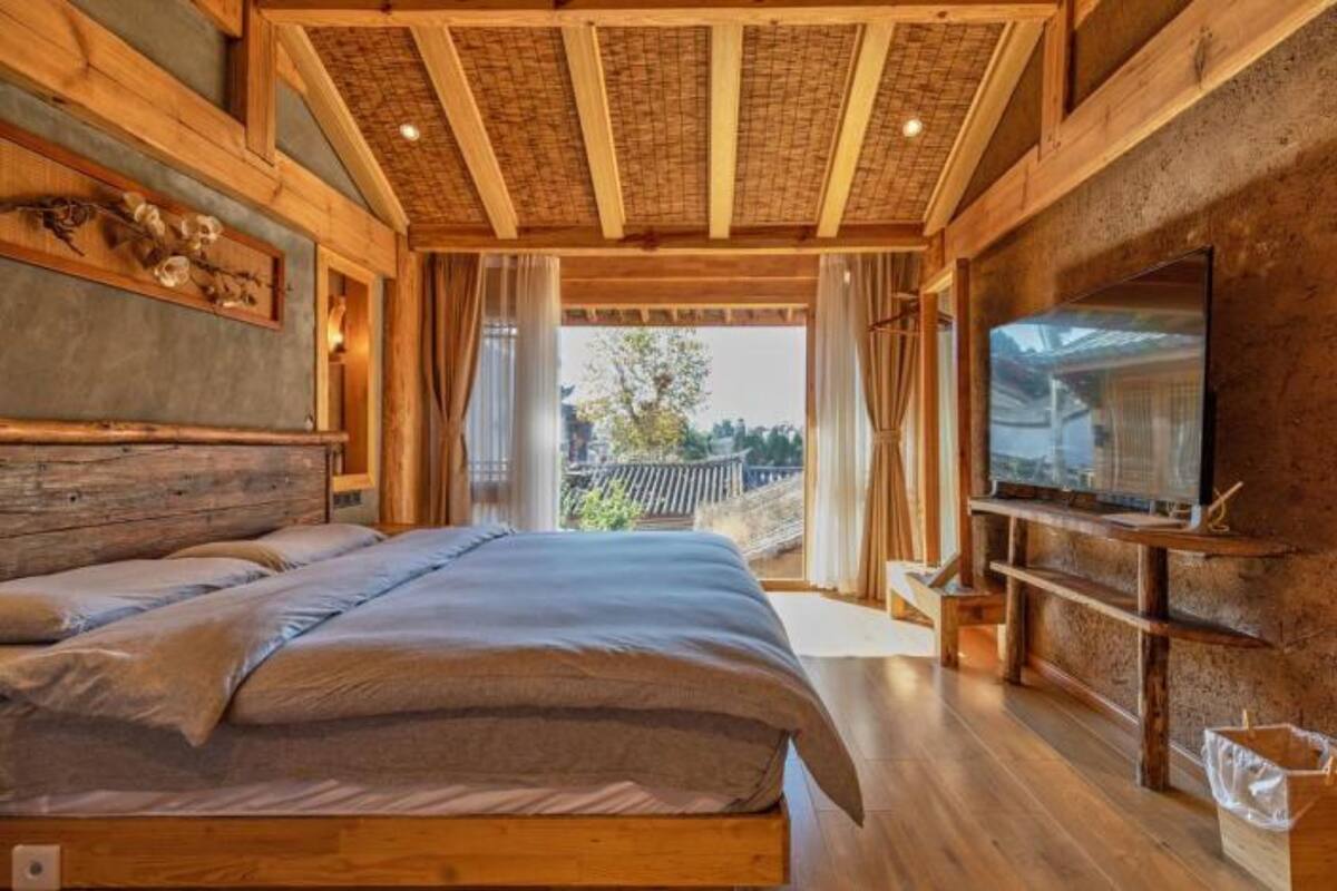 A wooden bedroom with a large bed, a TV on a wooden stand, and a balcony with a view.