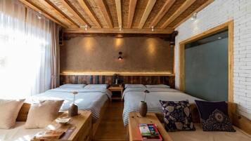 A room with two beds, wooden beams on the ceiling, a brick wall, and a large window with curtains.