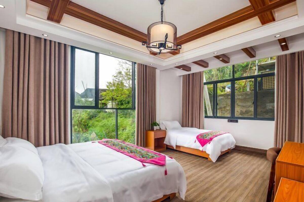 Ein Hotelzimmer mit zwei Betten, großen Fenstern, Holzboden und einer Decke mit sichtbaren Balken.