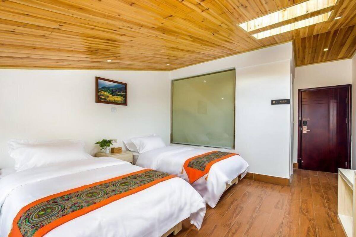 Ein Hotelzimmer mit zwei Betten, Holzboden, einem großen Fenster und einer Tür.