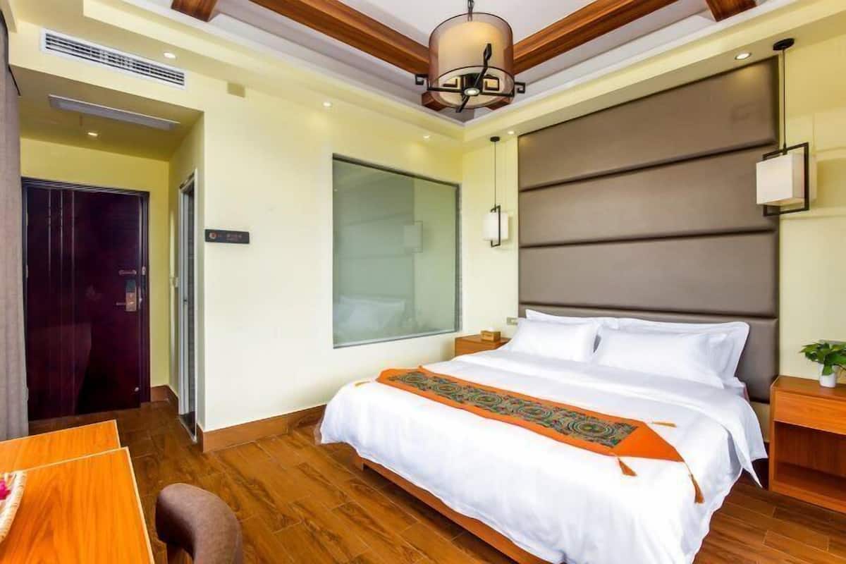Ein modernes Hotelzimmer mit einem großen Bett, Holzboden, einem großen Fenster und einer Decke mit Holzbalken.