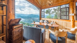 A wooden cabin with a large window offering a mountain view, a wooden table, and a radio. - Floral Hotel Longsheng Yueshangshanshe (Guilin)