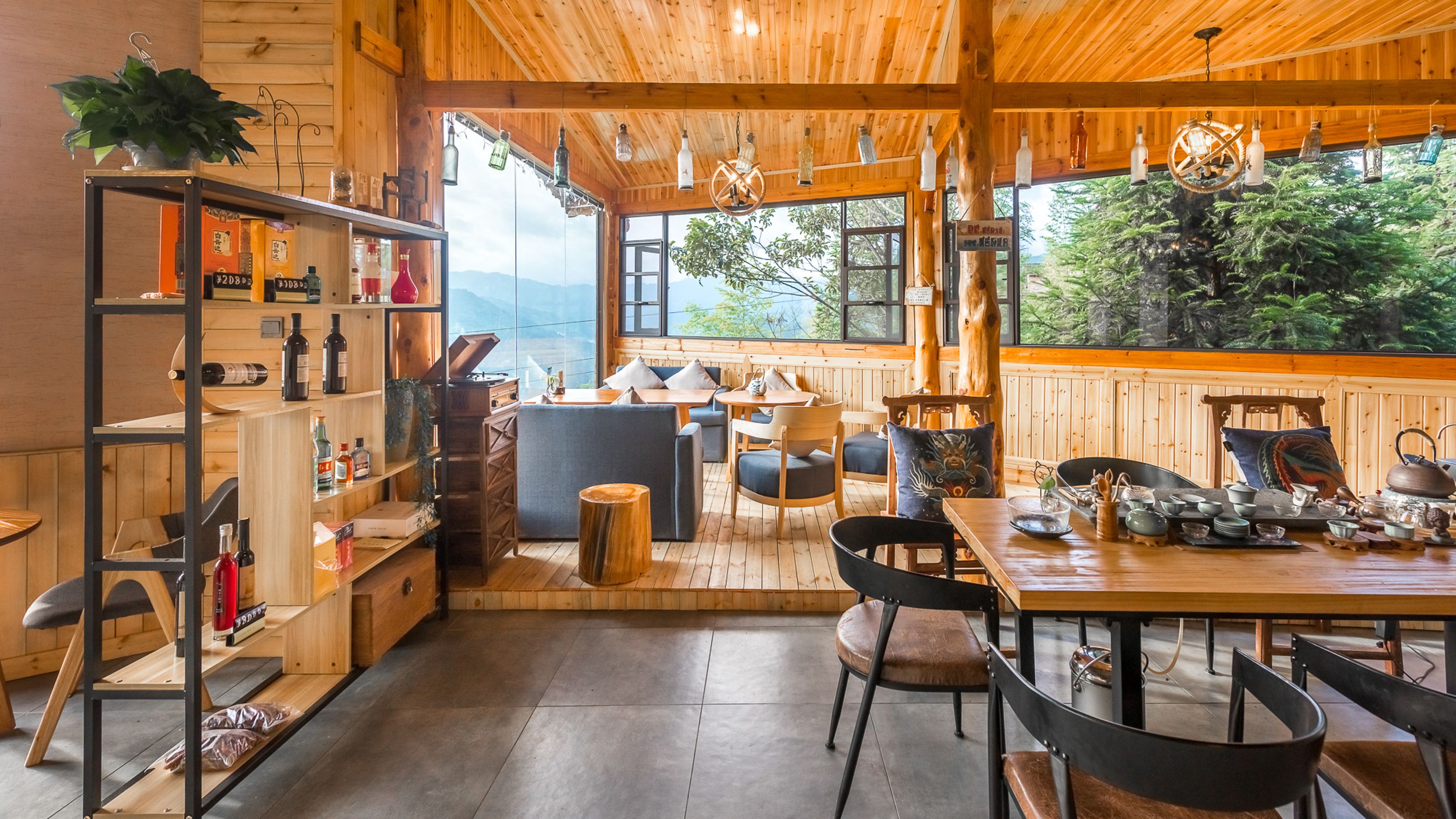 Interior de madera con zona de comedor, estantes con botellas y vistas a árboles.