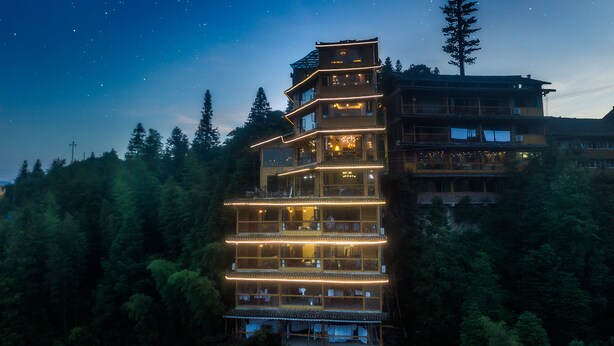 A multi-story hotel with balconies and a forested backdrop. - Floral Hotel Longsheng Yueshangshanshe (Guilin)
