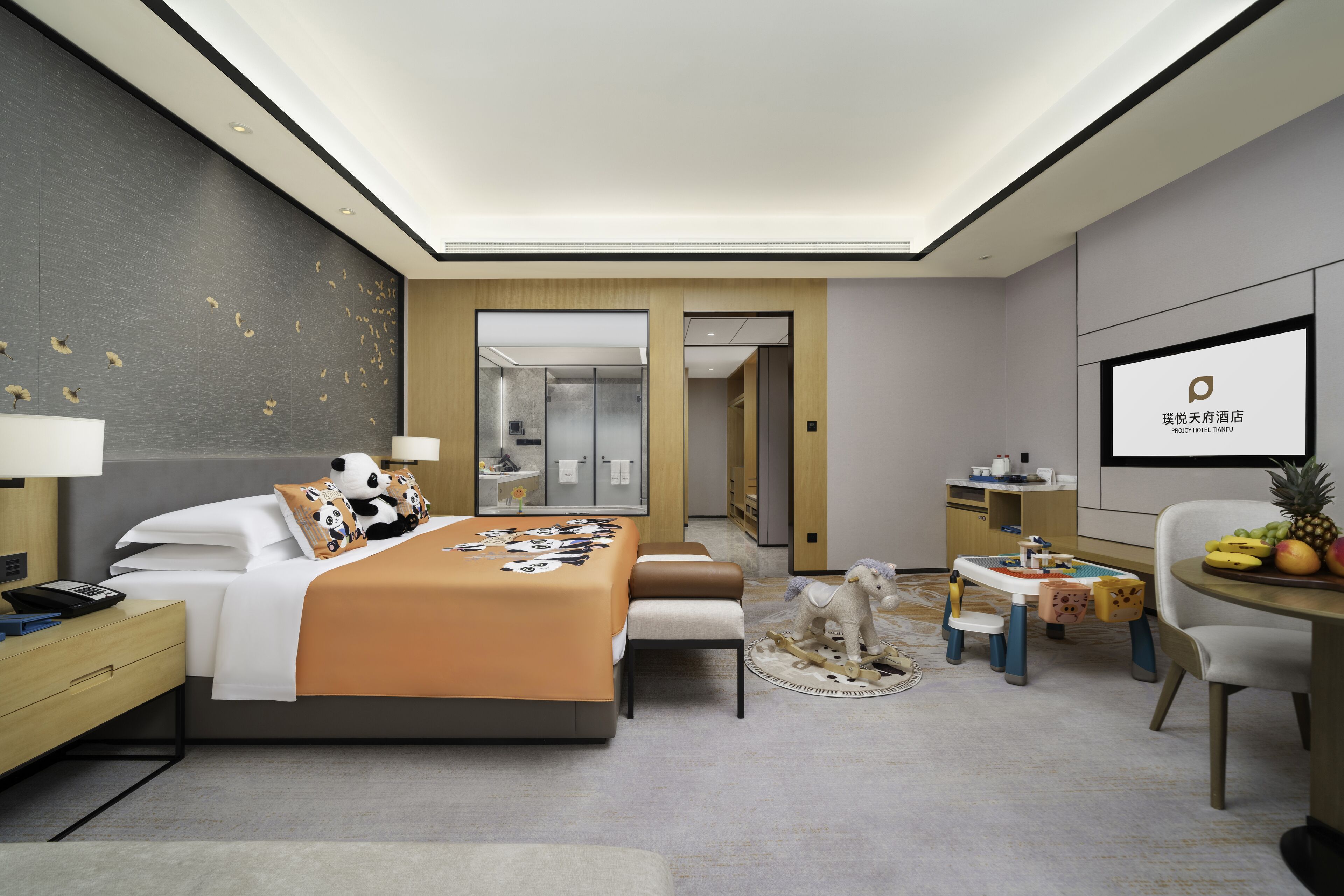 Une chambre d’hôtel moderne avec un grand lit, un bureau, une chaise, une petite table avec des fruits et un téléviseur fixé au mur.