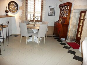 A dining area with a wooden table and four chairs, a wall clock, a window with blinds, and a cabinet with dishes. - THE SAINT PERE SANCERRE LOGISTIC