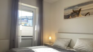 A bedroom with a bed, a nightstand, a lamp, a window with curtains, and a painting on the wall. - The "Seehase" in Haus Meeresglück, close to the beach and central! (Dahme)