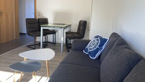 A modern living room with a grey sofa, a small white table, and two black chairs. - The "Seehase" in Haus Meeresglück, close to the beach and central! (Dahme)