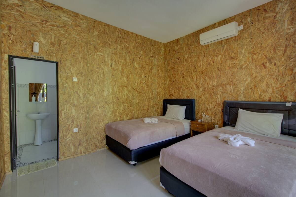 A hotel room with two beds, a bathroom with a sink, and a no-smoking sign on the wall.