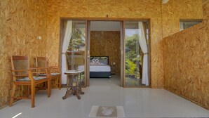 Une pièce comprenant un lit, une table et deux chaises. Une porte vitrée donne sur un balcon agrémenté de plantes.
