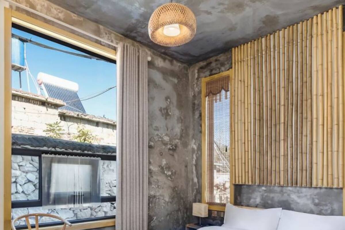 Un dormitorio con una cama grande, una silla de madera, una mesita de noche, una lámpara y vistas al exterior.