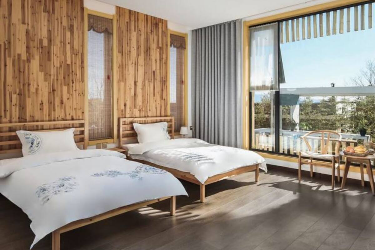 Un dormitorio moderno con dos camas de madera, un ventanal con cortinas y un balcón con mesa y sillas.