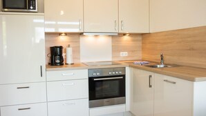 A modern kitchen with white cabinets, a Bosch oven, a coffee maker, and a microwave. - "Sanddorn" in the Strandburg house... close to the beach and in a quiet location! (Dahme)