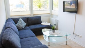 A modern living room with a grey sectional sofa, a glass coffee table, and a flat-screen TV mounted on the wall. - "Sanddorn" in the Strandburg house... close to the beach and in a quiet location! (Dahme)