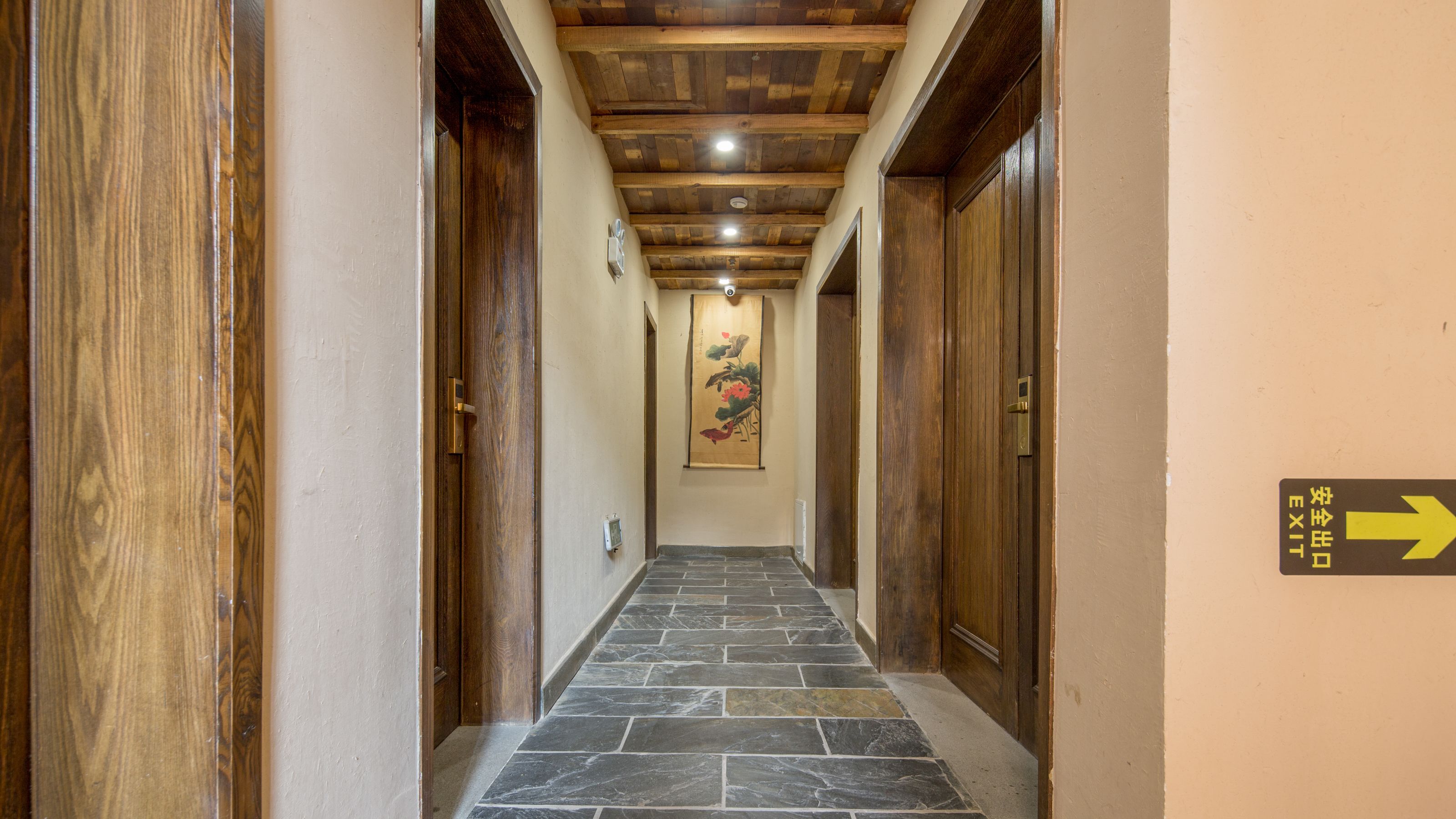 Un pasillo con puertas de madera, suelo de baldosas de piedra y una obra de arte colgada.