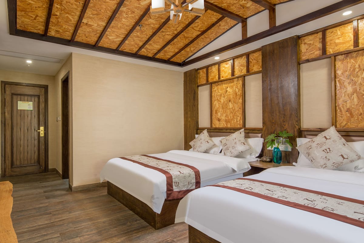 Habitación de hotel con dos camas, suelo y techo de madera, y un ventanal con paneles de madera.