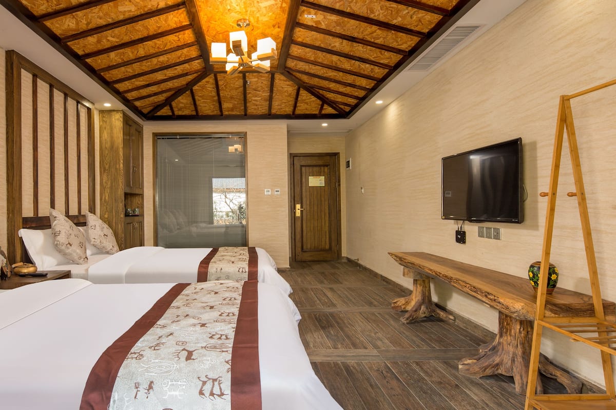 Habitación de hotel con dos camas, techo de madera, televisor y un banco.