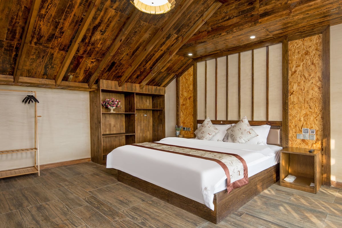 Un dormitorio con techo de madera, una cama grande con ropa blanca de cama, un armario de madera y una mesita de noche pequeña.