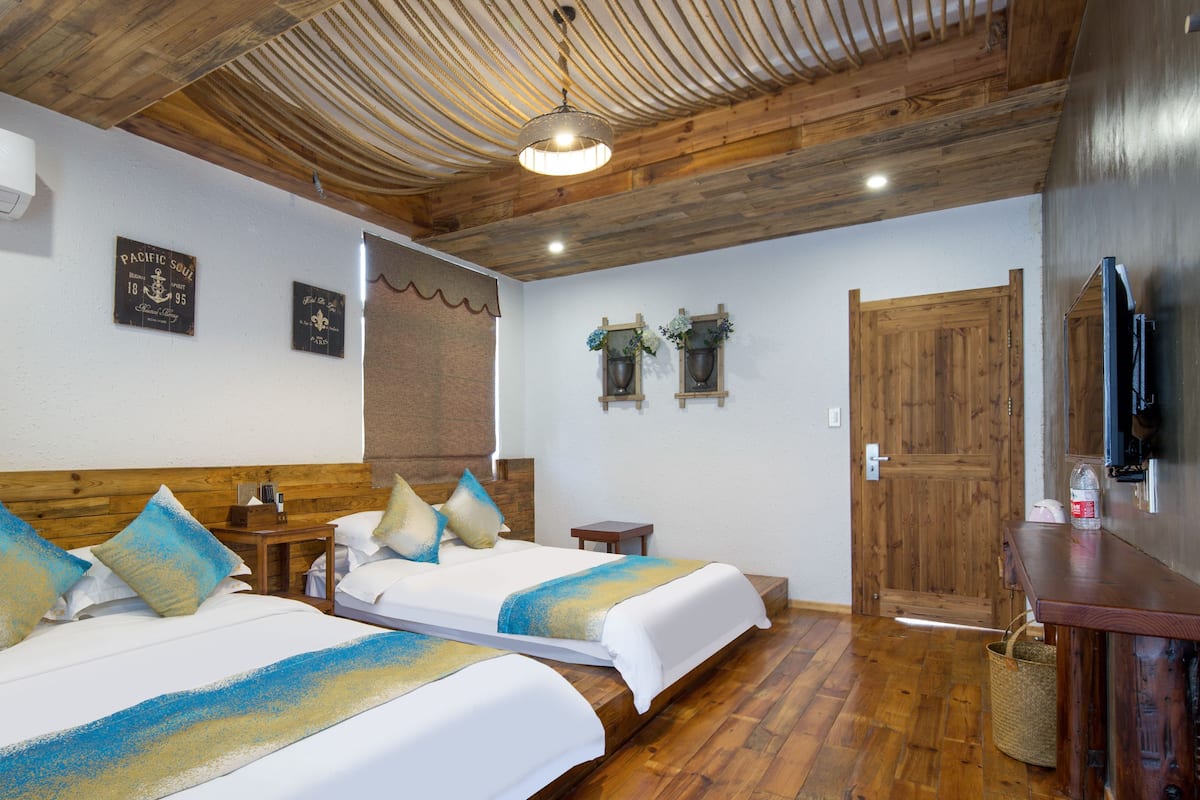 Habitación de hotel con dos camas, suelo y techo de madera, televisor y una puerta.
