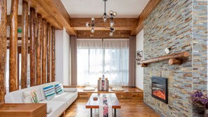 Un salon moderne avec une cheminée en pierre, des poutres en bois et une grande fenêtre ornée de rideaux légers.
