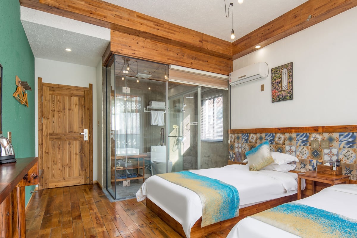 Un dormitorio con dos camas, cabina de ducha de vidrio, piso de madera y una pared verde.