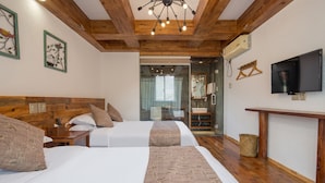 Une chambre d’hôtel avec deux lits, une tête de lit en bois, une télévision et une salle de bain visible à travers une porte en verre.