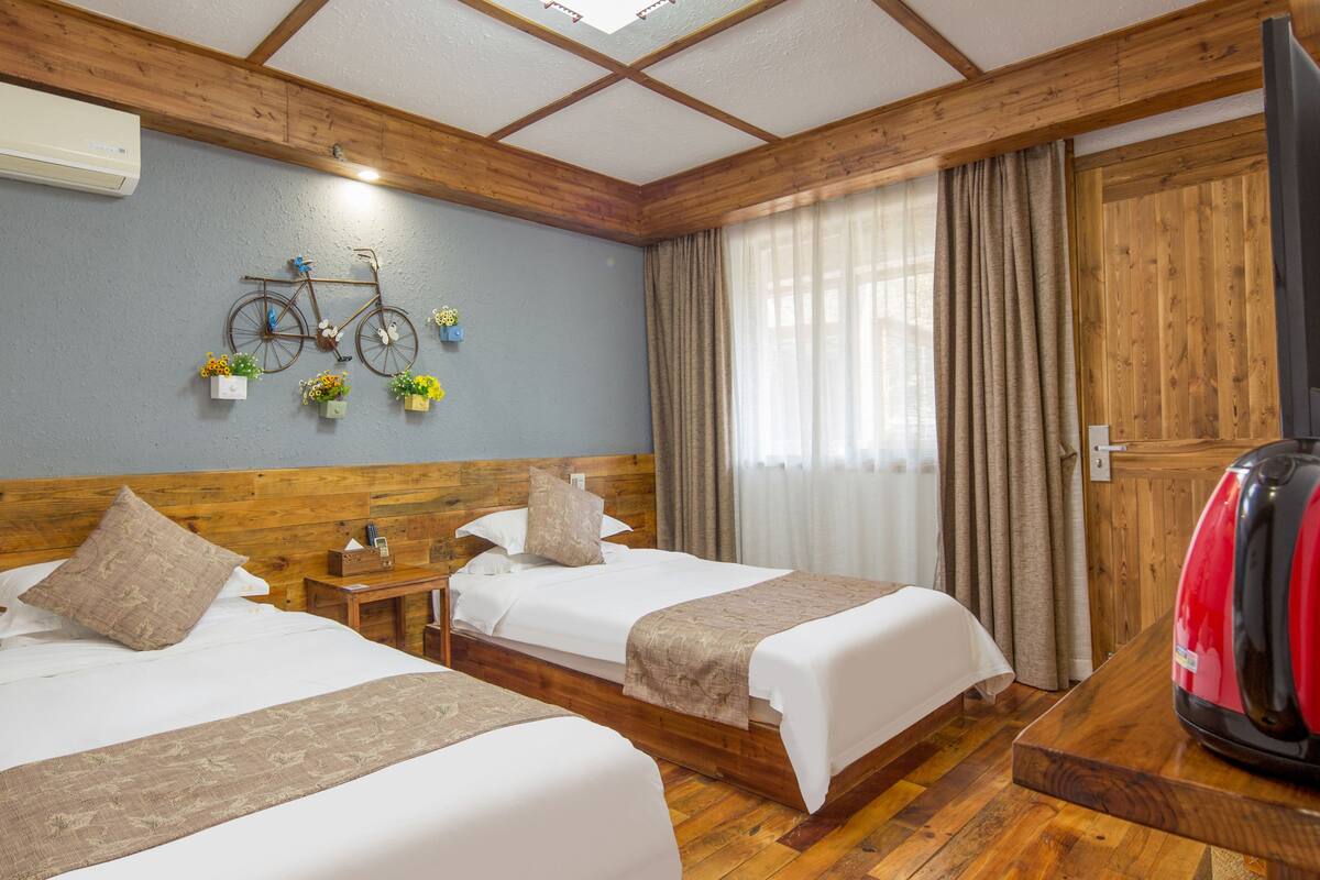 Habitación de hotel con dos camas, cabeceros de madera, un adorno con forma de bicicleta, un televisor y una maleta roja.