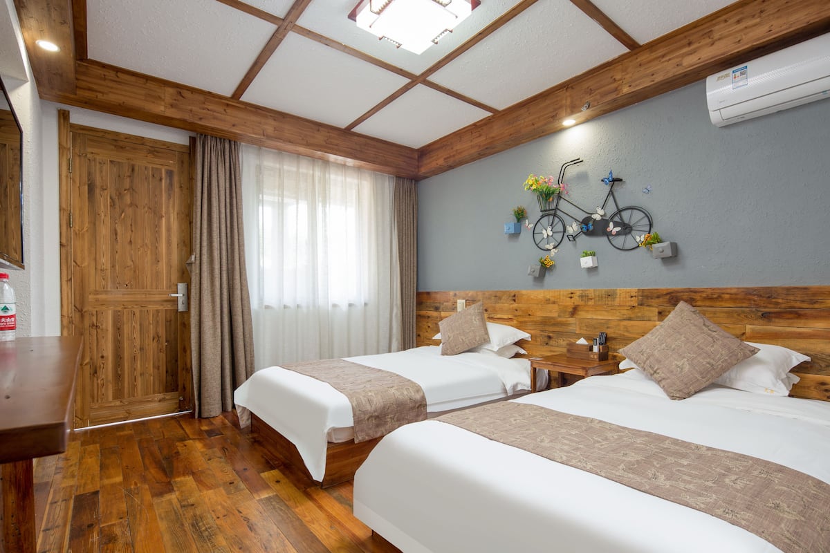 Habitación de hotel con dos camas, piso de madera, cabecero de madera, una bicicleta como adorno en la pared y una ventana con cortinas.