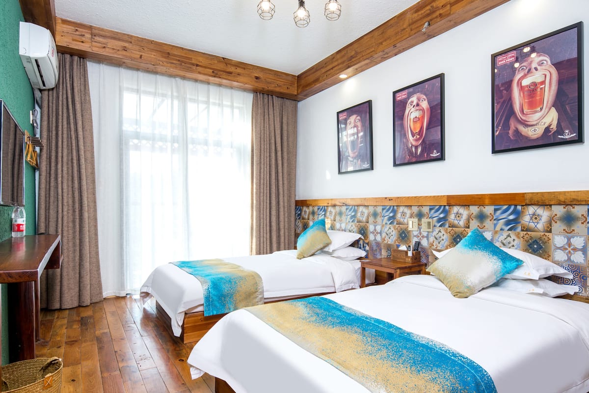 Habitación de hotel con dos camas, cabecero de madera, un escritorio con computadora y un ventanal con cortinas.