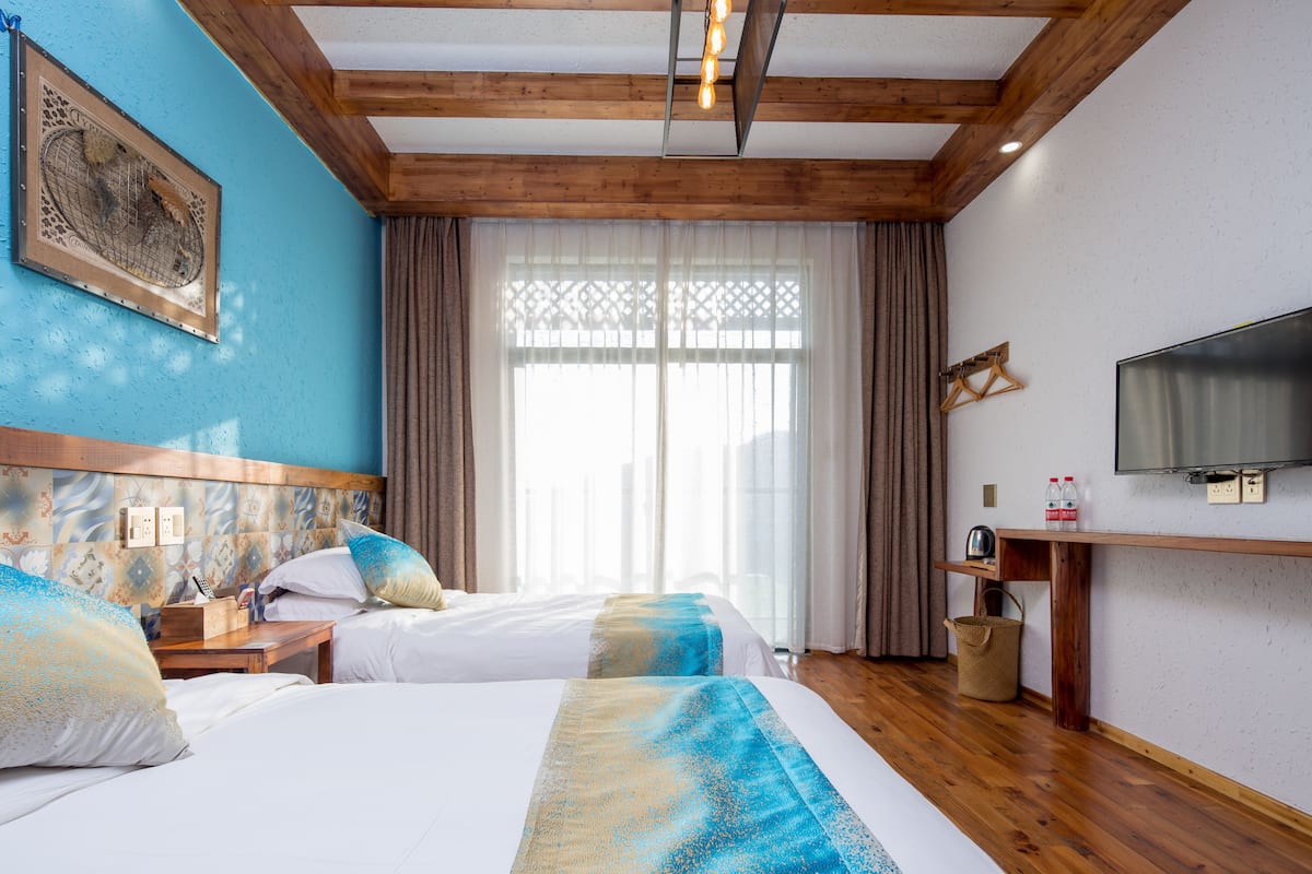 Habitación de hotel con dos camas, televisión, escritorio y ventana con cortinas.