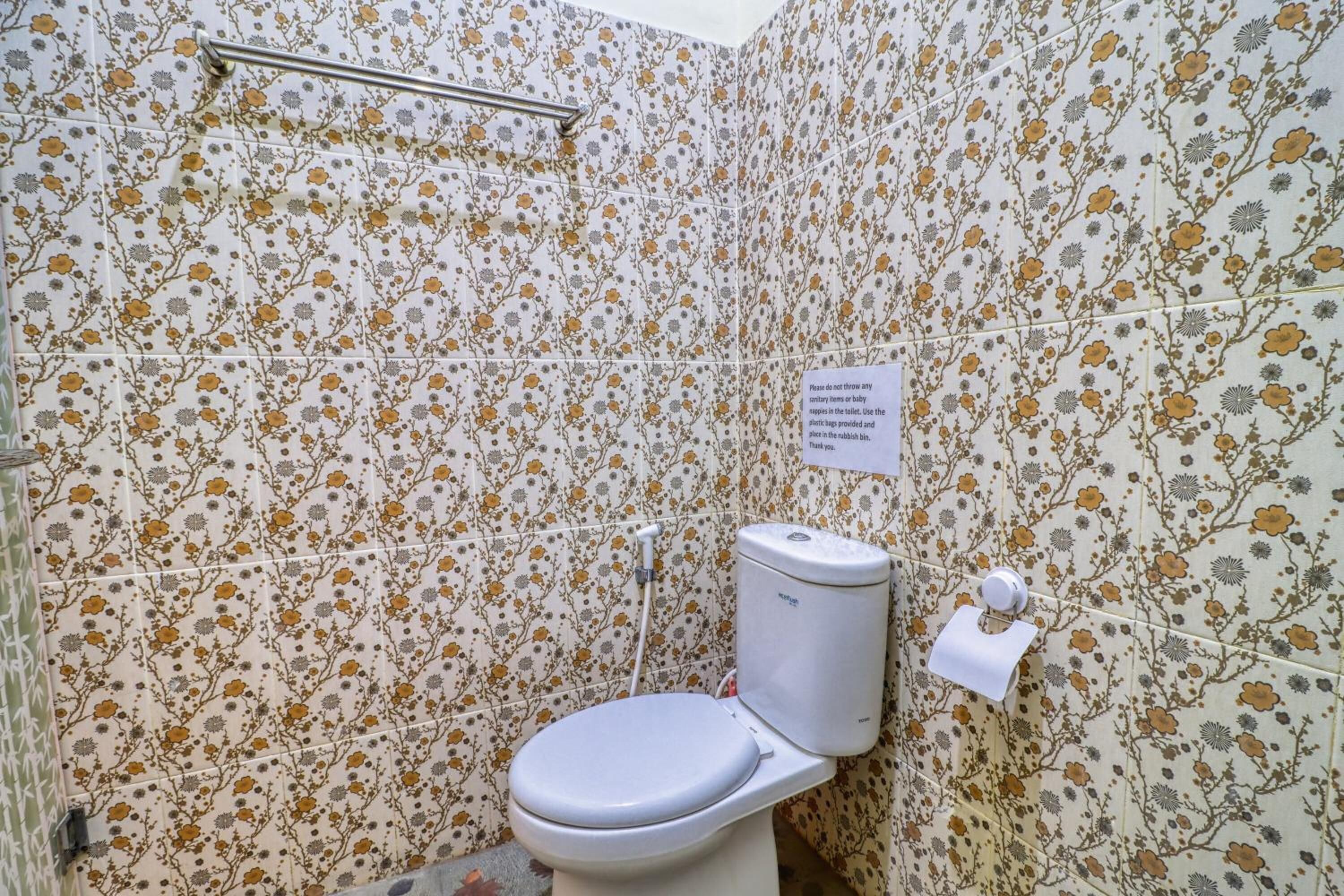 Ein Badezimmer mit Fliesen in floralem Muster, einer weißen Toilette, einer Haltestange und einem Papierhandtuchspender.