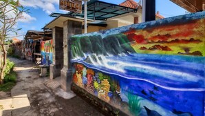 A colorful mural on a building's exterior wall depicting a tropical scene with waterfalls and marine life. - Nibugi Guest House (Penida Island)