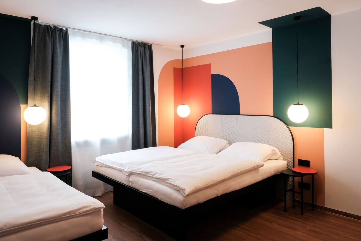 A modern hotel room with a large bed, a smaller bed, and a desk with a chair.