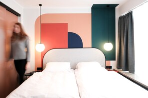 A modern hotel room with a bed, bedside tables, and a large window with curtains. - The Dot - 24-7 Check-in (Munich)