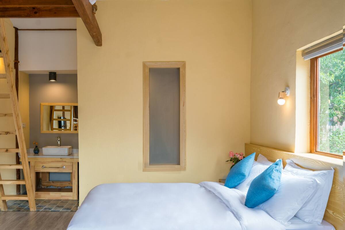 A bedroom with a wooden ladder, a built-in sink, a bedside table, and a window with a view.