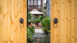 Um portão de madeira que dá para um jardim com um pequeno elemento aquático e vasos de plantas.
