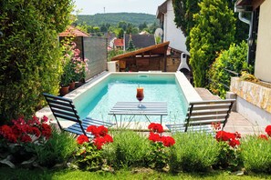 Ein Schwimmbecken mit einem Glas Rotwein, umgeben von roten Blumen und Grünpflanzen.
