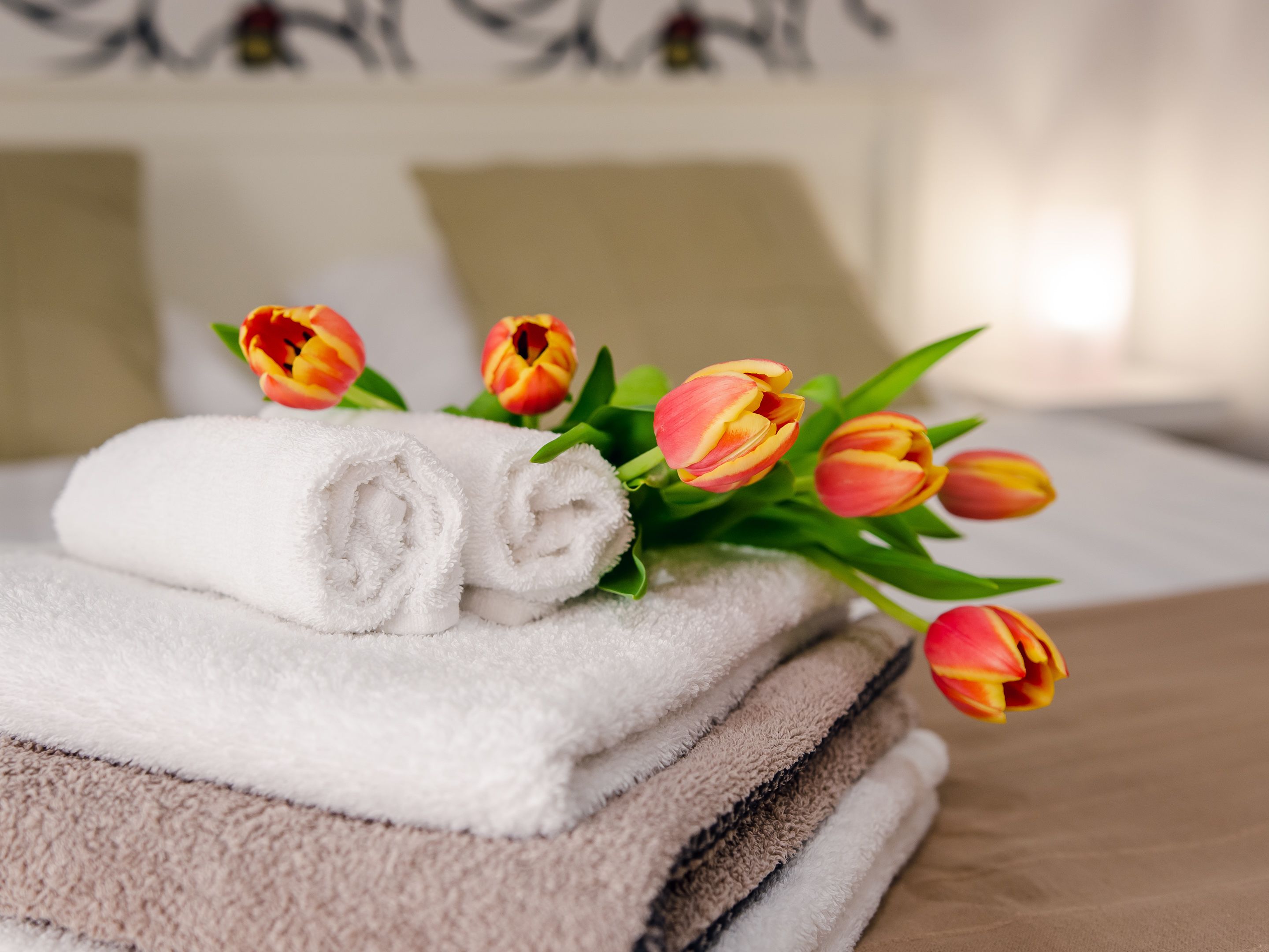 A stack of neatly folded towels and a bouquet of tulips on a bed.